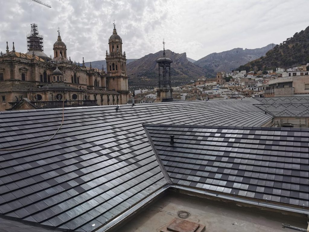 Cubierta recién rehabilitada con teja plana sobre edificio histórico, con vista de la Catedral de Jaén al fondo.