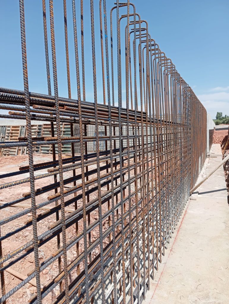 Estructura de acero corrugado utilizada para la construcción de un muro de contención. Se observa la armadura vertical y horizontal antes del encofrado, en un entorno de obra urbana o civil.